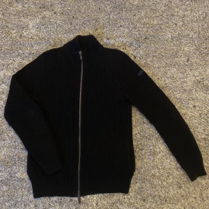 Svart stickad tröja från Hugo Boss - Snygg svart stickad tröja från Hugo Boss med dubbel dragkedja framtill. Väldigt kraftigt material som håller värmen bra, perfekt nu under vintern eller tidig vår/sen höst. Var lite slarvig när jag hängde upp den så bosslappen på insidan lossnade lite (se bild). Dock inget som syns utåt 🙌 2499:- nypris. Om du önskar ytterligare info eller specifika bilder så är det bara att skriva 🙏