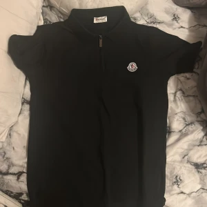 Svart kortärmad topp från Moncler - Snygg svart kortärmad topp från Moncler med dragkedja framtill och klassisk krage. Perfekt för en stilren look. Moncler-logga på bröstet ger en exklusiv touch.