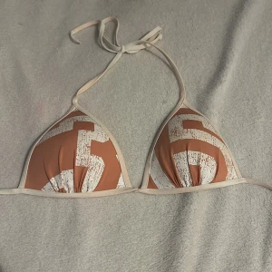 Rosa och vit bikiniöverdel från H&M - Snygg bikiniöverdel från H&M i rosa med vita detaljer. Triangelformad design med knytband i nacken och ryggen. Perfekt för en dag på stranden eller vid poolen.