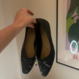 Svarta ballerinaskor med rosett - Säljer ett par eleganta svarta ballerinaskor med en söt rosett på tån. Perfekta för en stilren look och bekväma att bära hela dagen.