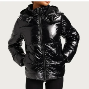 Svart glansig pufferjacka - Snygg svart pufferjacka med glansig finish och dragkedja framtill. Jackan har en huva med snörning och långa ärmar. Perfekt för kyligare dagar.