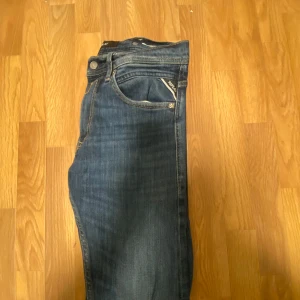 Blå jeans från Replay - Snygga blå jeans från Replay med klassisk femficksdesign och knappgylf. Jeansen har en mörk tvätt och subtila slitningar för en trendig look. Perfekta för en avslappnad stil.