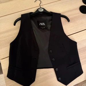 Svart väst från Zara ” Aldrig använt ” - Snygg svart väst från Zara med knappar framtill. Perfekt för en stilren look. Västen har en klassisk design och är lätt att matcha med olika outfits.