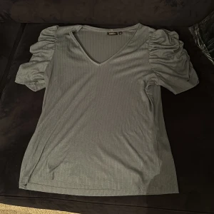 Grå ribbad topp från KappAhl - Säljer en stilren grå ribbad topp från KappAhl med puffiga kortärmar och v-ringning. Perfekt för en avslappnad men chic look. Passar bra till både jeans och kjol.