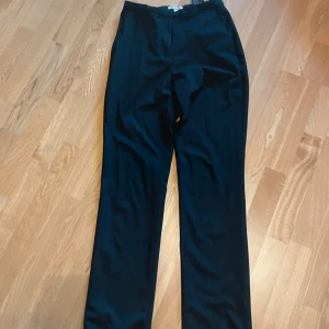 Svarta kostymbyxor - Snygga svarta kostymbyxor med hög midja och rak passform. Perfekta för en stilren look. Byxorna har en enkel design utan synliga detaljer och är tillverkade i ett mjukt material som ger en bekväm känsla.