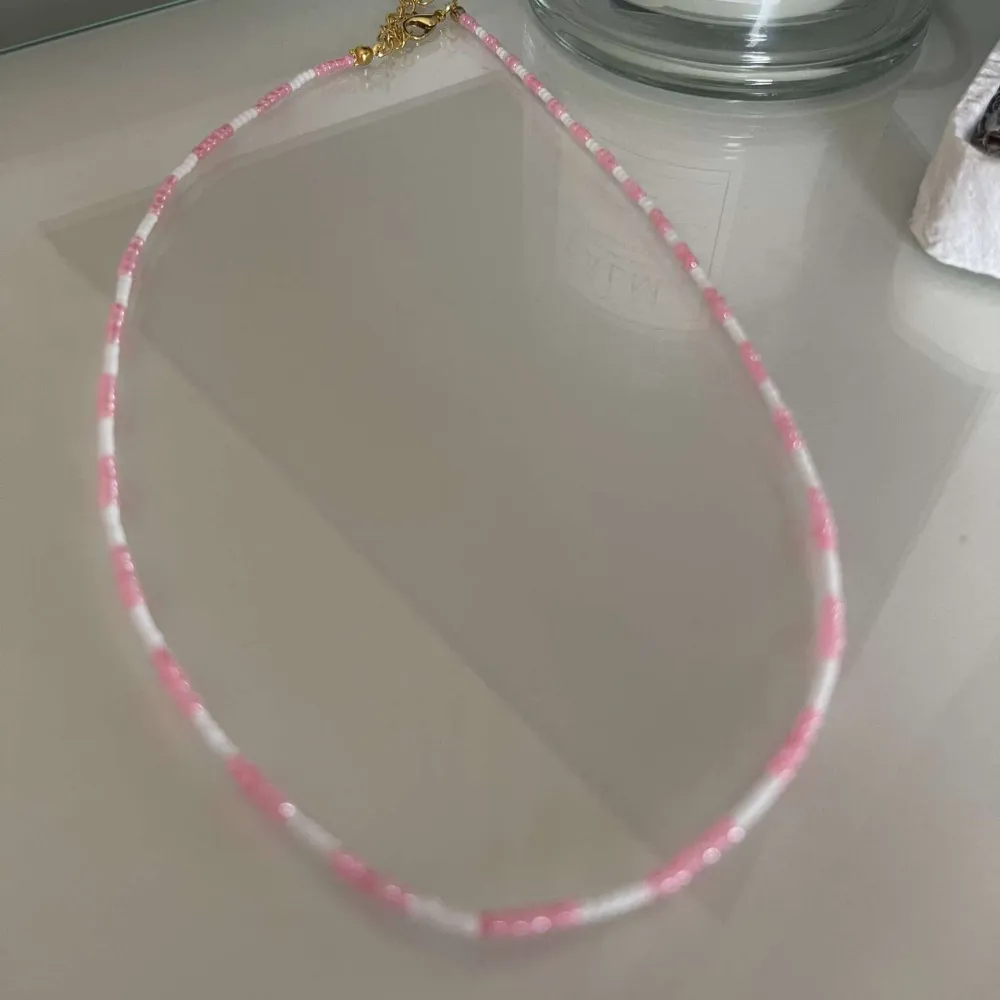 Säljer ett supergulligt halsband med små rosa och vita pärlor. Perfekt för att ge en söt touch till vilken outfit som helst. Halsbandet har ett guldigt lås som ger en fin kontrast till de ljusa pärlorna. Passar perfekt till sommarens alla fester och tillfällen! 🌸. Accessoarer.