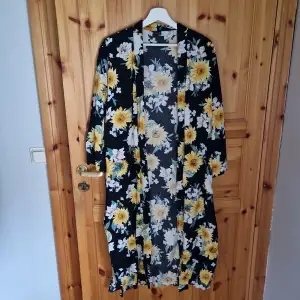 Säljer en superfin lång kimono med ett blommigt mönster i gult och vitt på en svart bakgrund. Den har trekvartsärmar och ett knytband i midjan. Perfekt för sommarens fester eller som en snygg detalj över en enkel outfit!