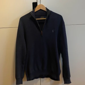 Mörkblå tröja från Polo Ralph Lauren - Säljer en snygg mörkblå tröja från Polo Ralph Lauren i Pima Cotton. Tröjan har en dragkedja vid halsen och är perfekt för både höst och vinter. Den är långärmad och har en stilren design med en liten logga på bröstet. Perfekt för en casual men ändå uppklädd look!