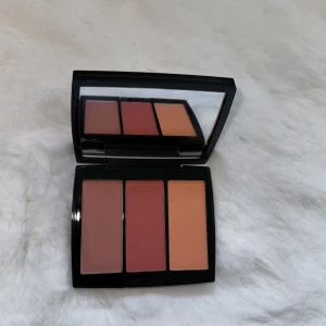 Blush Trio Peachy Love från Anastasia Beverly Hills - Säljer en superfin Blush Trio i nyansen Peachy Love från Anastasia Beverly Hills. Den innehåller tre olika rougefärger: en mjuk persikoton, en djupare rosa och en varm orange. Perfekt för att ge kinderna en fräsch och livfull look! Kompakt och lätt att ta med sig, med en praktisk spegel i locket.