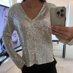 Glittrig tröja - Superfin v-ringad glittrig tröja i champagne färg från Bikbok i storlek Xs som passar olika festliga tillfällen. Använd bara en gång så tröjan är i nyskick!