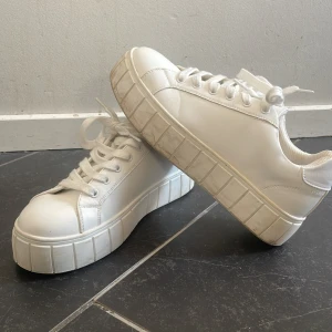Vita sneakers med platåsula - Säljer ett par vita sneakers med en rejäl platåsula. De har snörning och är i syntetmaterial. Perfekta för att ge lite extra höjd och stil till din outfit. Använda men i bra skick. Köpta på skopunkten