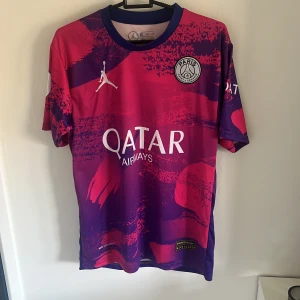Paris Saint-Germain fotbollströja - Säljer en cool Paris Saint-Germain fotbollströja i lila och rosa med Messi 10 på ryggen. Tröjan är kortärmad och har Qatar Airways som sponsor på framsidan. Den är i nyskick och har en unik design med Jordan-loggan på bröstet.