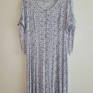 Blommig långklänning med knytärmar - Säljer en superfin långklänning med blått blommönster på vit bakgrund. Klänningen har korta ärmar med en snygg knytdetalj och en v-ringad hals. Perfekt för sommarens alla fester eller en avslappnad dag i solen!