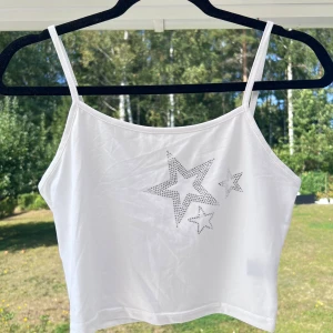 Vitt linne med strass - Ett vitt linne med smala axelband och strass-detalj på bröstet. Linnet är normalt i storleken. Säljer pga att det är lite för stort för mig. Aldrig använt 😚  Längd: 40 cm Byst: 78 cm