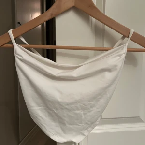 Vit axelbandslös topp - Säljer en stilren vit axelbandslös topp med knytning i ryggen. Perfekt för varma sommardagar eller en kväll ute. Enkel och elegant design som passar till det mesta.