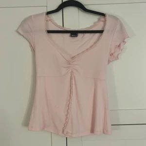 Ljusrosa topp från Gina Tricot - Säljer en söt ljusrosa topp från Gina Tricot med v-ringning och korta ärmar. Toppen har fina spetsdetaljer, använd fåtal gånger och är i väldigt bra skick. Strl S, passar en 13 åring tjej!!