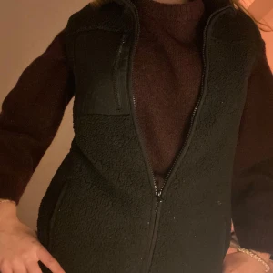 Svart fleeceväst - Säljer en svart fleeceväst med dragkedja framtill. Perfekt för kyligare dagar och enkel att matcha med olika outfits.