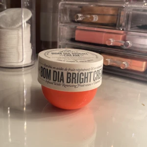Bom Dia Bright Cream från Sol de Janeiro - Bom Dia Bright Cream i en livlig orange burk med vitt lock. Krämen är designad för att ge huden en hälsosammare, mjukare och ljusare look. Innehåller fruktsyror och vitamin C för att förbättra hudens textur och utseende.