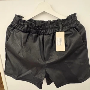 Svarta shorts i skinnimitation - Snygga svarta shorts i skinnimitation med elastisk midja. Perfekta för en trendig look. Passar bra till både vardag och fest.