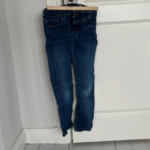 Blå jeans från Lindex - Säljer ett par snygga blå jeans från Lindex i storlek 146. De har en smal passform och klassisk femficksdesign. Perfekta för vardagsbruk!