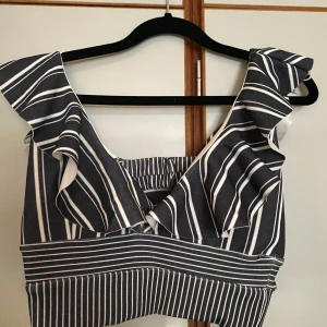 Randig volangtopp - Snygg randig topp med volangdetaljer. Den har en croppad passform och är perfekt för sommarens varma dagar. Toppen har en djup v-ringning och breda axelband. Toppen är supersnygg, tyvärr så är etiketten avklippta pga skav därav vet jag inte exakt storlek, men chansar på xs/s. 