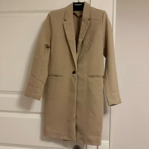 Beige kappa från Gina Tricot - Snygg beige kappa från Gina Tricot i storlek 34. Den har en klassisk design med knappar framtill. Perfekt för en stilren look.