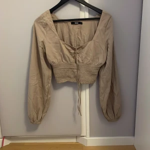 Beige blus från Bik Bok - Snygg beige blus från Bik Bok med långa ärmar och knytning framtill. Perfekt för en stilren look. Vi kan komma till ett rimlig pris tillsammans 