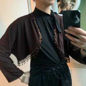 Brun bolero med pärldetaljer - Snygg brun bolero från InWear med pärldetaljer längs kanterna. Perfekt för att ge en extra touch till din outfit. Långärmad och i en elegant design.