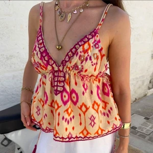 Topp från Zara - Säljer en färgglad linne topp med v-ringning och smala axelband. Toppen har ett livfullt mönster i rosa och orange med dekorativa knytband framtill och i ryggen. Perfekt för sommardagar!Aldrig använd så i nyskick💕Storlek M men passar S