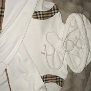 Vit hoodie från Burberry - Säljer en stilren ÄKTA vit hoodie från Burberry med klassiska rutiga detaljer på sidorna och insidan av huvan. Tröjan har en luva med snöre. Köpt på NK för 1 år sedan för ca 5000kr