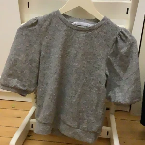 Grå tröja från 157 - Säljer en stilren grå tröja från 157 i storlek XS. Tröjan har puffiga trekvartsärmar och en rund halsringning. Perfekt för en avslappnad look. Passar även för mindre storlekar.