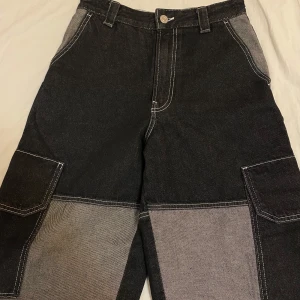 Svarta cargopants från Bershka - Snygga svarta cargopants från Bershka med kontrasterande sömmar och stora fickor. Byxorna har en loose passform och är perfekta för en avslappnad stil. Tillverkade i ett slitstarkt material med knapp och dragkedja framtill.