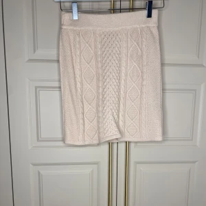 Beige stickad kjol från Bubbleroom - Snygg beige stickad kjol från Bubbleroom med ett detaljerat flätmönster. Kjolen har en elastisk midja för extra komfort och är perfekt för kyligare dagar.