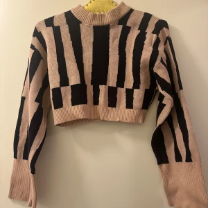 Randig croppad tröja från Monki - Säljer en cool randig tröja från Monki i beige och svart. Tröjan är croppad med långa ärmar och har en ribbad halsringning. Perfekt för en trendig look!