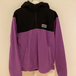 Svart och lila fleecejacka med huva - Säljer en mysig fleecejacka från Junkyard i svart och lila. Jackan har en praktisk huva och dragkedja framtill. Perfekt för kyliga dagar! Köptes i november så som ny 💕