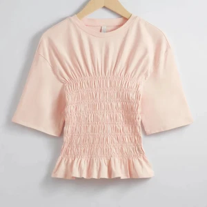 Ljusrosa topp med smockdetaljer - Säljer en söt ljusrosa topp med smockdetaljer i midjan och volangkant. Toppen har korta ärmar och en rund halsringning. Perfekt för en avslappnad stil. SKRIV TILL MIG INNAN DU KLICKAR PÅ KÖP! 💞💞