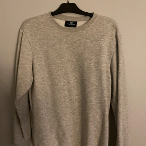 Grå sweatshirt från H&M - Säljer en grå sweatshirt från H&M med rund hals och avslappnad passform. Perfekt för en bekväm och stilren look. Tröjan har långa ärmar och är tillverkad i ett mjukt material.