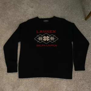 Mörkblå tröja från Ralph Lauren - Säljer en svart tröja från Ralph Lauren med ett snyggt mönster i rött och vitt på framsidan. Tröjan är långärmad och tillverkad i 100% bomull, perfekt för kyligare dagar.