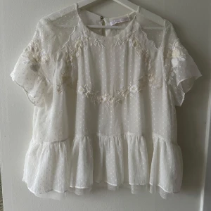 Vit blus med spetsdetaljer - Charmig vit blus från Zara med spetsdetaljer och prickigt mönster. Blusen har korta ärmar och volangdetaljer vid nederkanten. 