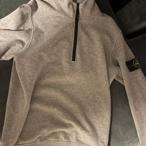 Grå tröja med dragkedja från Stone Island - Säljer en snygg grå tröja från Stone Island i storlek S. Tröjan är i mycket bra skick, ändats används ett fåtal gånger. Tröjan har halv dragkedja och lång ärm. Tröjan passar perfekt i alla årstider. Den är såklart äkta. Kan diskutera ett bra pris vid snabb affär. Nypris 3000 kr.