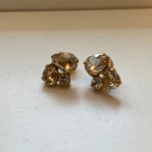 Guldiga örhängen med kristaller - Eleganta guldiga örhängen prydda med gnistrande kristaller i olika storlekar. Perfekta för att ge en touch av glamour till din outfit.