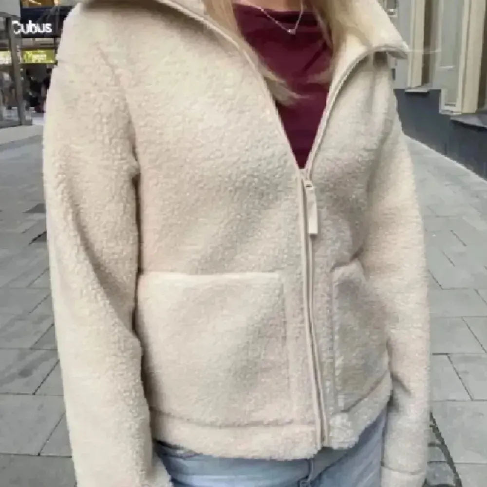 Mysig beige teddyjacka med dragkedja framtill och hög krage. Perfekt för kyliga dagar och ger en trendig look. Jackan har en normal passform och är lätt att matcha med olika outfits. Helt ny med prislappen kvar.. Takit.