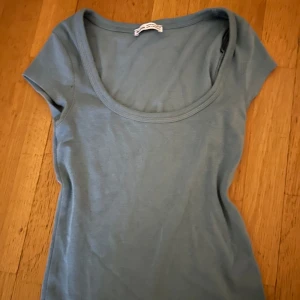 Blå kortärmad topp från Bershka - Säljer en stilren blå topp från Bershka i storlek XS. Toppen har en rund halsringning och korta ärmar, perfekt för en avslappnad look.