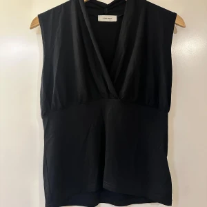 Svart ärmlös topp från Vera Moda - Snygg svart ärmlös topp från Vera Moda med djup v-ringning. Perfekt för en stilren look. Tillverkad i ett mjukt material som ger en bekväm passform.🌟