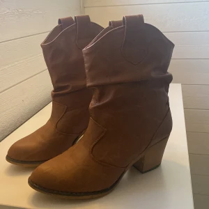 Bruna cowboy boots med klack - Snygga bruna cowboy boots med klack och rundad tå. Perfekta för en stilren look. Tillverkade i ett material som liknar skinn.
