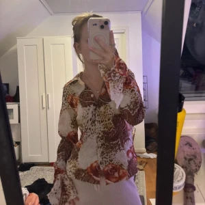 Mönstrad blus från BiBA - Säljer en unik blus från BiBA med ett djärvt mönster i leopard och blommor. Blusen har långa ärmar och en klassisk krage. Perfekt för att ge din outfit en färgklick!