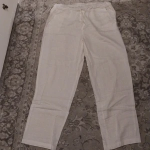 Vita linnebyxor från Zabaione - Säljer ett par vita linnebyxor från Zabaione i storlek M. Byxorna har en avslappnad passform med resår i midjan och snörning för extra komfort. Perfekta för en somrig look!