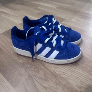 Blå Adidas Campus - Snygga blå sneakers från Adidas med vita ränder och snörning. Skorna har en klassisk design med en bekväm sula och är perfekta för vardagsbruk. Tillverkade i mocka för en stilren look. Adidas campus i storlek 42. Pris 900 kr