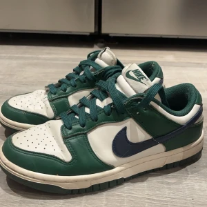 Nike Dunk i grönt,vit & mörkblå - Säljer nu mina snygga Nike Dunk sneakers i grönt och vitt med blå swoosh. Skorna har klassisk snörning och perforerad tå för extra ventilation. Perfekta för en stilren look. Storlek 37,5, bara att höra av dig vid frågor. Pris kan diskuteras!💗