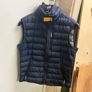 Mörkblå dunväst från Parajumpers - Säljer en mörkblå quiltad dunväst från Parajumpers. Västen har dragkedja och en gul detalj vid halsen. Perfekt för lager-på-lager under kyliga dagar. Barnstorlek!!